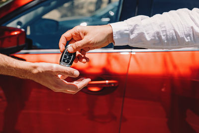 Dealer giving car keys to the new owner. close-up of hands on the background of red automobile