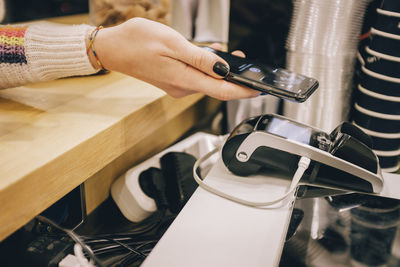 High angle view of woman holding mobile phone over credit card reader on table