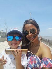 Portrait of smiling young woman wearing sunglasses against sky