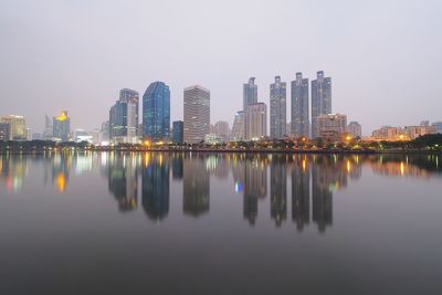 Reflection of modern buildings on river against sky in city