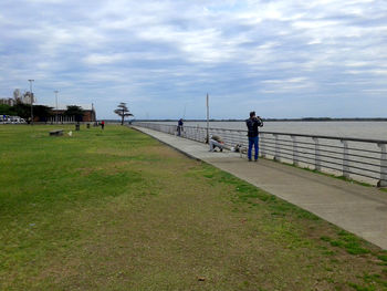 People walking on footpath by sea against sky