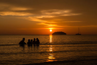 Silhouette people on sea against sky during sunset