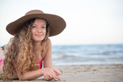 Portrait of woman wearing hat while lying at beach against clear sky