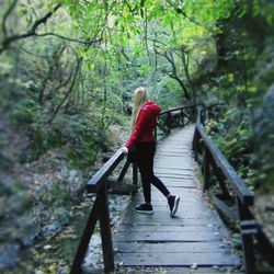 Woman standing on footbridge amidst trees at forest