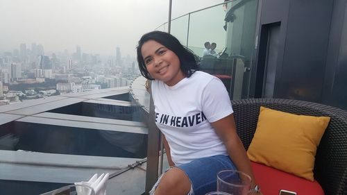 Woman smiling while sitting at restaurant against cityscape