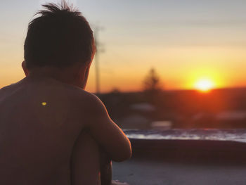 Rear view of shirtless man against sky during sunset