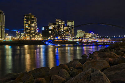 Illuminated city by river against sky at night