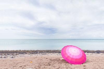 Pink umbrella on beach against sky