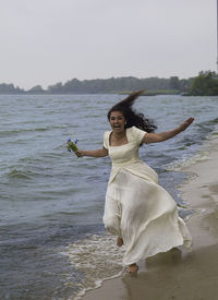 Woman with arms raised on beach against sky