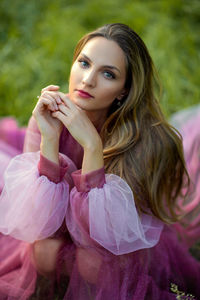 Portrait of young woman in a pink dreamy dress sitting in forest