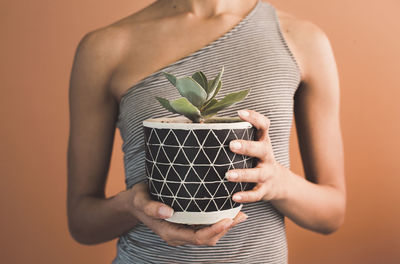 Midsection of woman holding potted plant against brown background