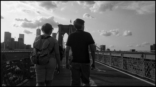 People standing on railing against cloudy sky