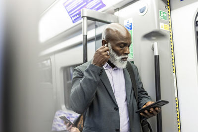 Businessman with smart phone wearing wireless in-ear headphones in train