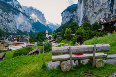 Rear view of woman sitting by buildings against mountains