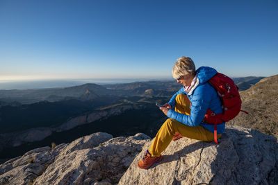 Young woman standing on rocks on top of a mountain with mobile phone.