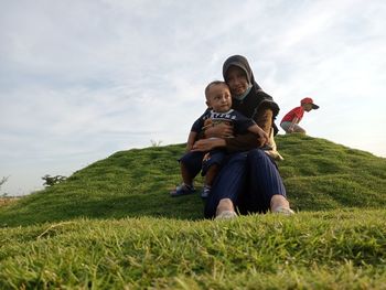 Full length of young woman sitting on field against sky