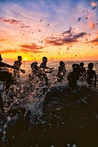 Silhouette people on beach against sky during sunset