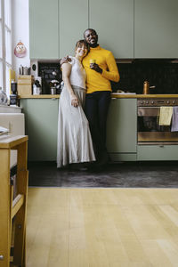 Full length portrait of couple standing together in kitchen at home