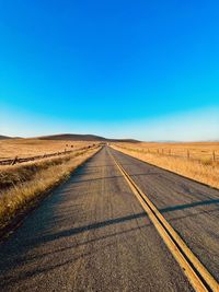 Road leading towards landscape against clear blue sky