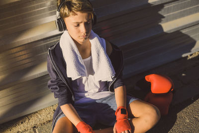 High angle view of boy sitting by wall while listening to music outdoors