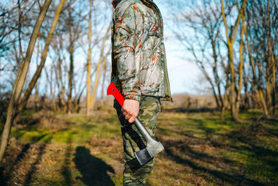 Person in camouflage clothing holding axe in the forest