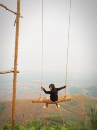 Rear view of boy swinging against sky