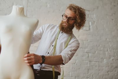 Fashion designer holding mannequin against wall