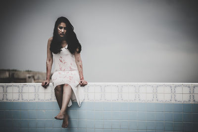 Full length of woman sitting on wall against sky