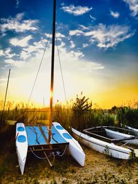 Sailboats moored on shore against cloudy sky during sunset