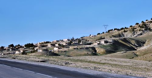 Road by buildings against clear blue sky