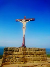 Low angle view of cross and jesus christ statue against clear blue sky