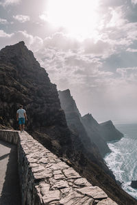 Low angle view of woman standing on cliff by sea against sky