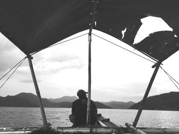 Rear view of man sitting on shore against sky