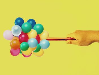Person holding multi colored balloons against yellow background