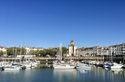 Sailboats moored in river by buildings against clear sky