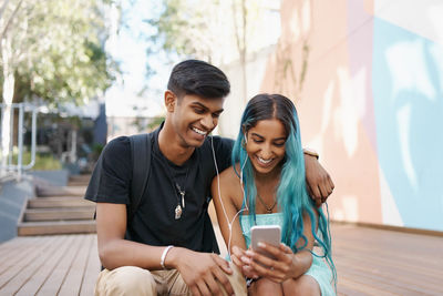 Happy friends using mobile phone while sitting outdoors