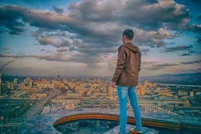 Rear view of man standing on rock at observation point against cloudy sky