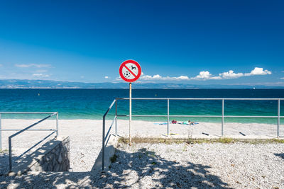 Information sign by sea against blue sky