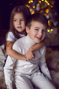 Girl hugs her brother sitting on bed in studio on christmas day