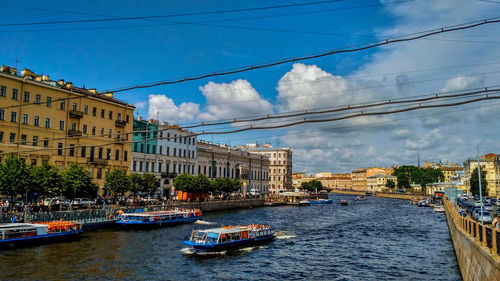 Boats in canal amidst buildings in city against sky