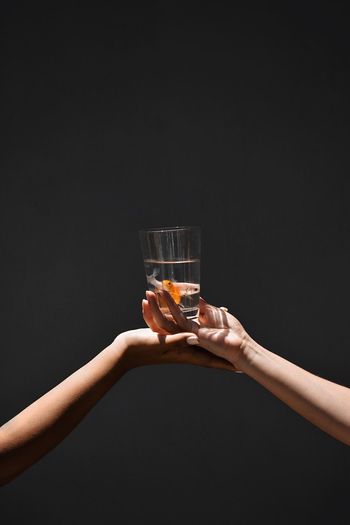 Cropped image of hands holding fishes in glass against black background
