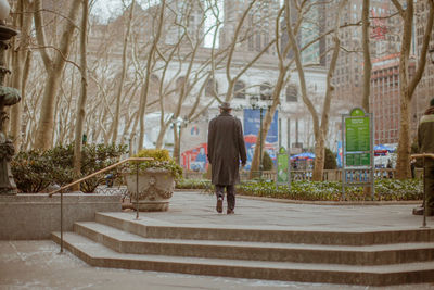 Full length of man walking in park against trees and buildings