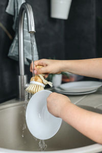 A child washes dishes with a wooden brush with natural bristles in the kitchen.