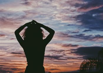 Silhouette woman with arms raised against cloudy sky during sunset