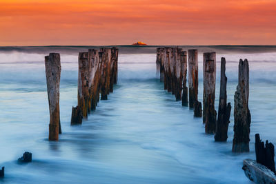 Wooden posts in sea against cloudy sky during sunset