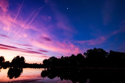 Reflection of silhouette trees in calm lake at sunset