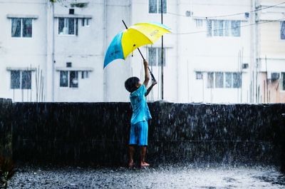Full length of boy holding umbrella standing in rain