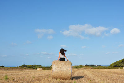 Rear view of woman sitting on field against sky