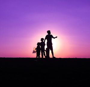 Silhouette children playing on field against sky during sunset