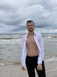 Portrait of young man standing at beach against sky